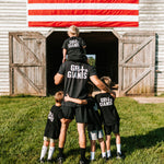 Father and four sons wearing black Grit & Giants shirts in front of a barn and American flag.