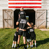 Father and four sons wearing black Grit & Giants shirts in front of a barn and American flag.