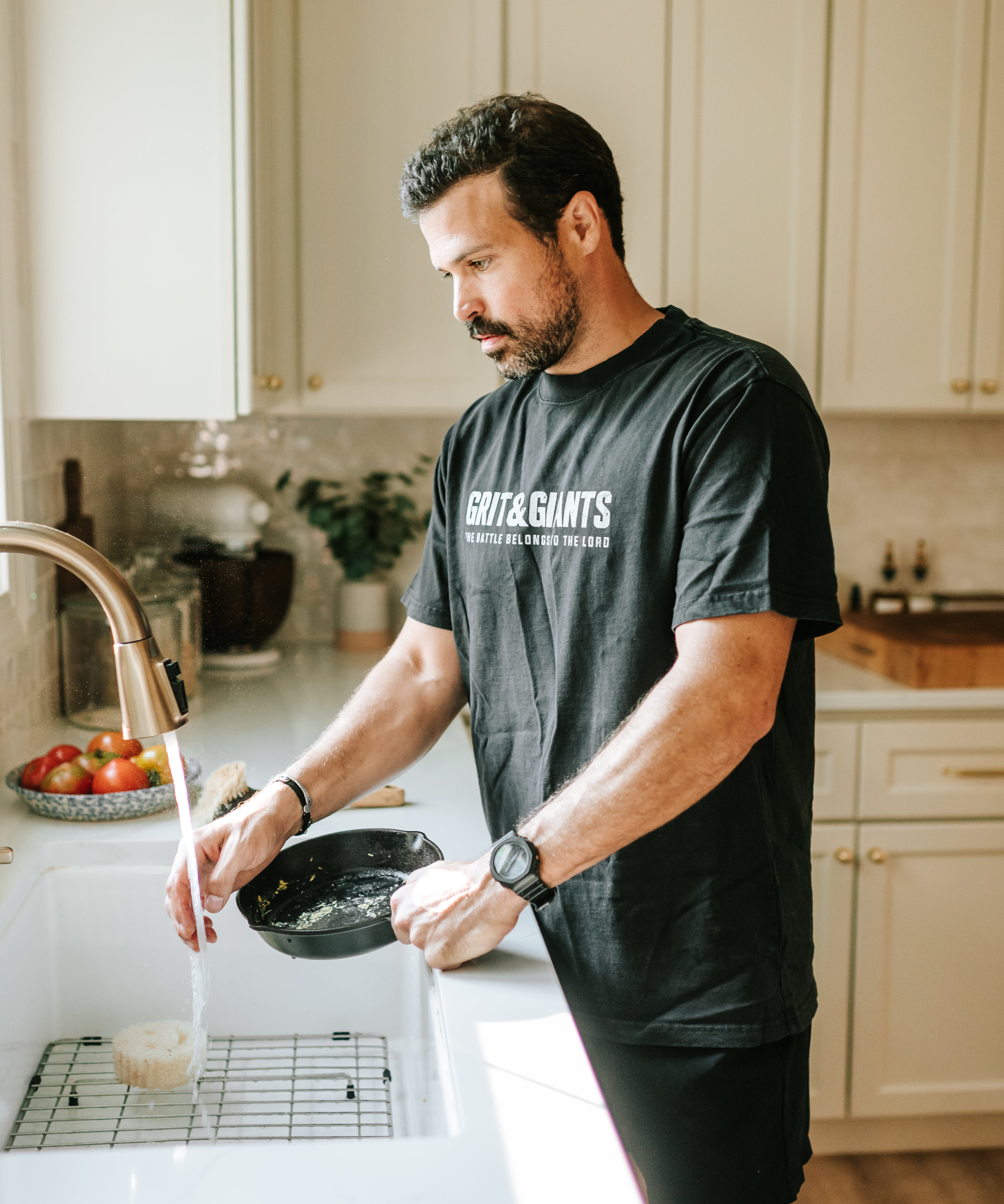 Man wearing a Faded Black Grit & Giants Heavyweight Tee while washing a cast iron skillet in the kitchen.