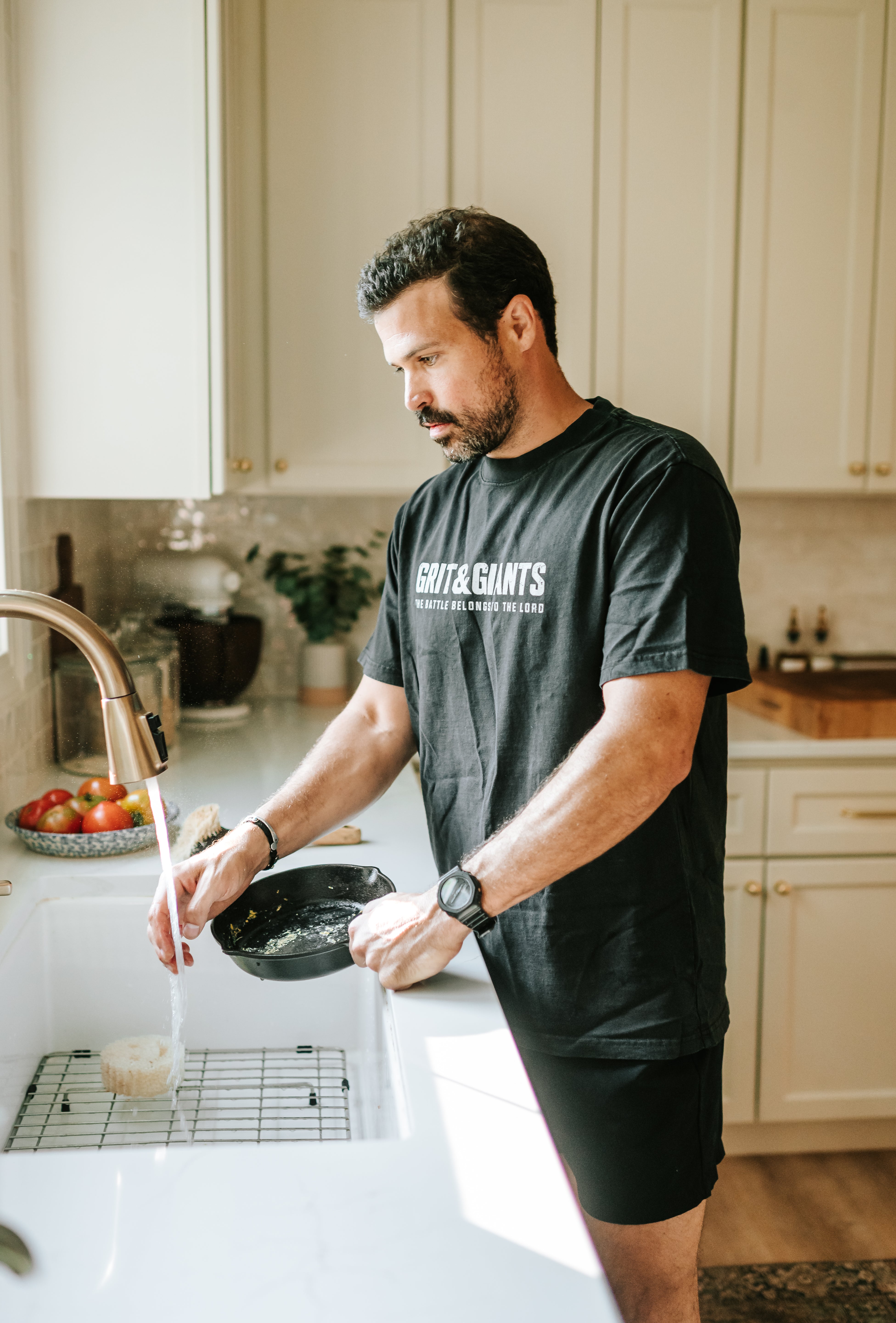 Man wearing a Faded Black Grit & Giants Heavyweight Tee while washing a cast iron skillet in the kitchen.