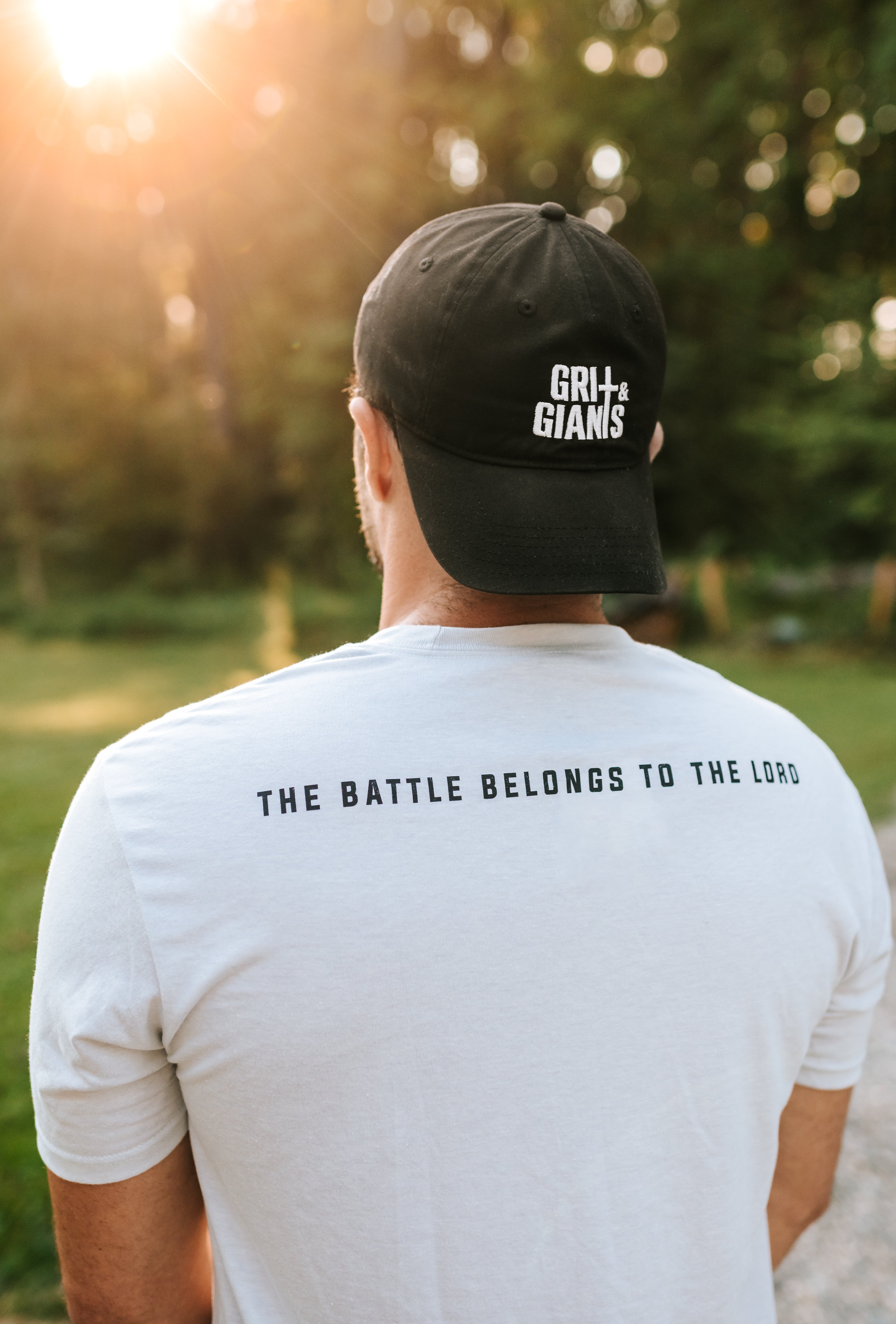 Back view of a man wearing the white smoke Grit & Giants Overcomer Training Tee featuring The Battle Belongs to the Lord.