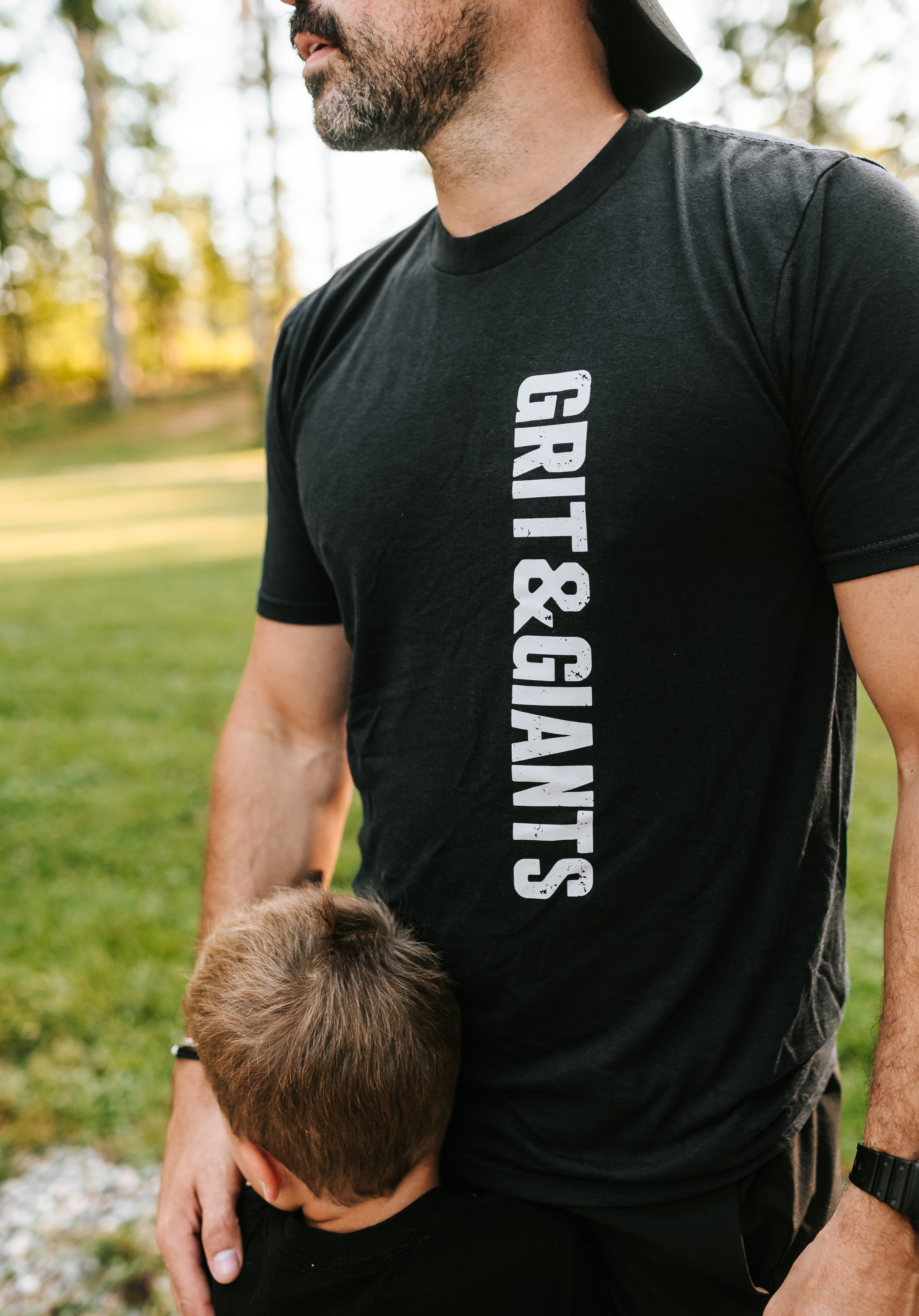 Father wearing a black Grit & Giants Refuge Training Tee outdoors with his son.