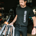 Man wearing a black Grit & Giants Refuge Training Tee while moving equipment in a garage.