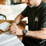 Man wearing a black Grit & Giants Signature Tee while reading the Bible during a morning devotional.