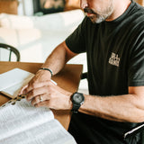 Man wearing a black Grit & Giants Signature Tee while reading the Bible during a morning devotional.