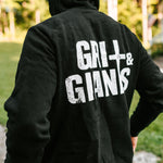 Back view of a man wearing a black Grit & Giants Stone Signature Hoodie outdoors.