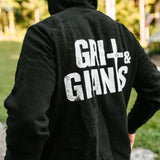 Back view of a man wearing a black Grit & Giants Stone Signature Hoodie outdoors.