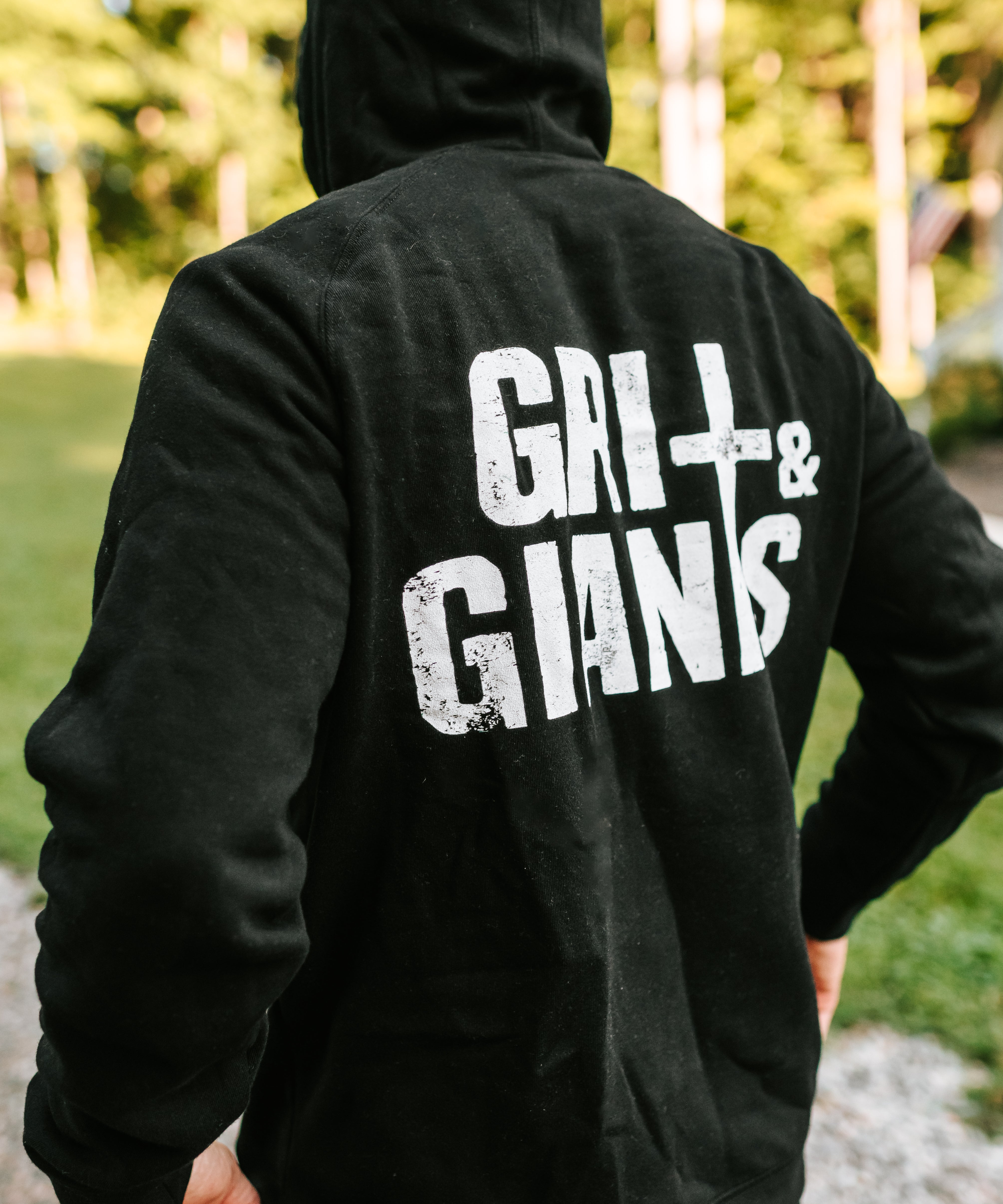 Back view of a man wearing a black Grit & Giants Stone Signature Hoodie outdoors.