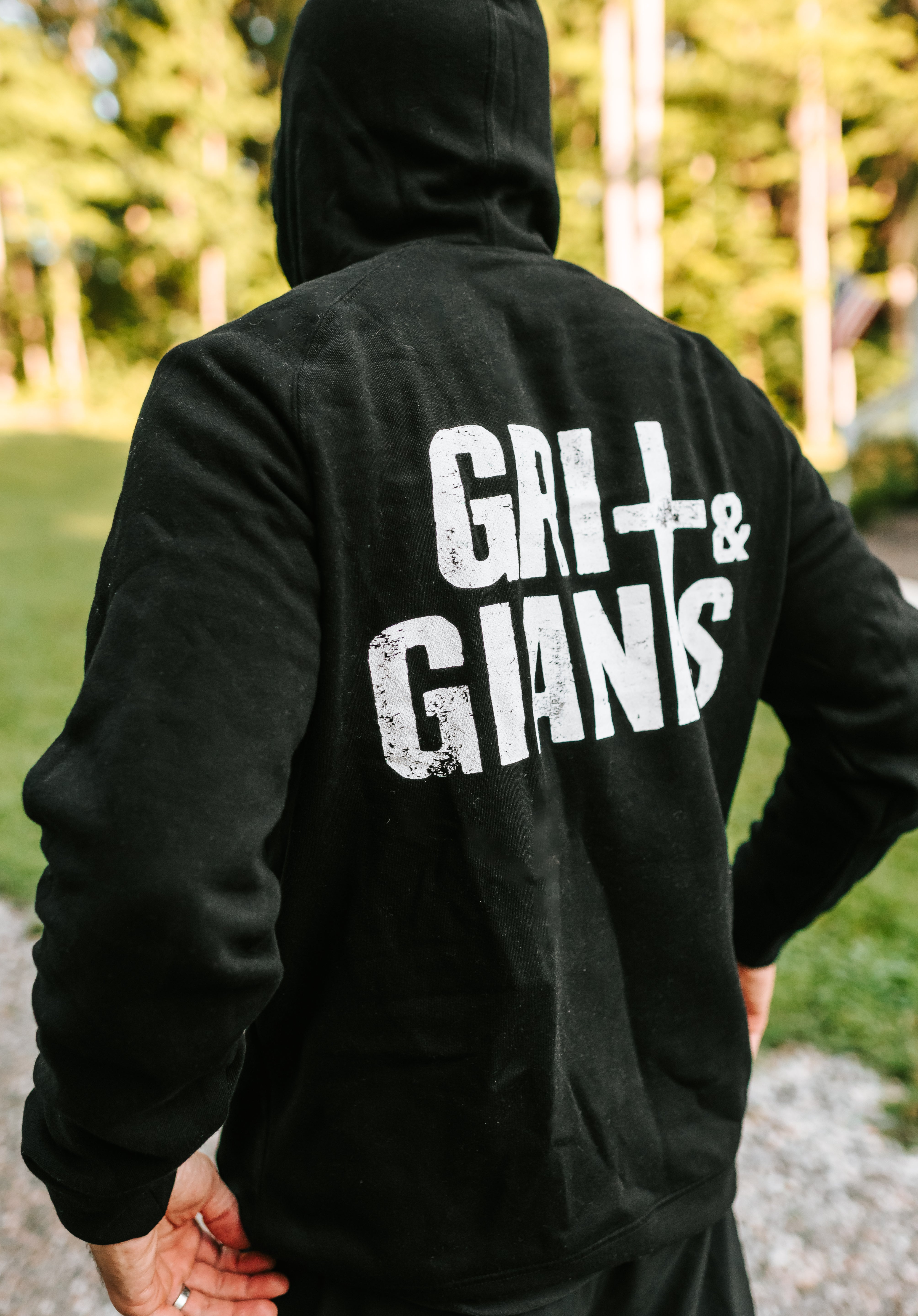 Back view of a man wearing a black Grit & Giants Stone Signature Hoodie outdoors.