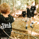 Boy wearing a black Grit & Giants toddler hoodie while exploring the woods.