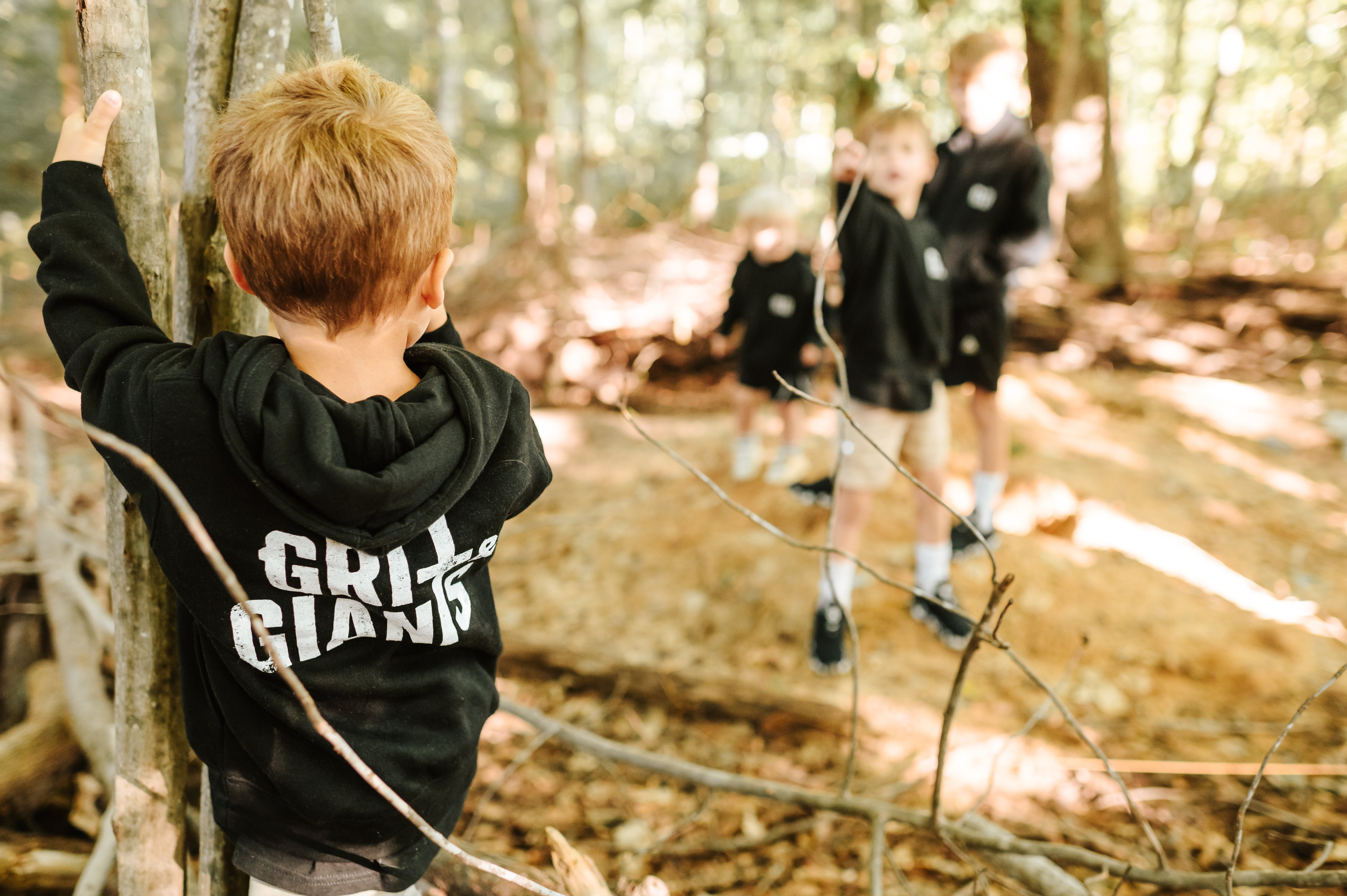 Boy wearing a black Grit & Giants toddler hoodie while exploring the woods.
