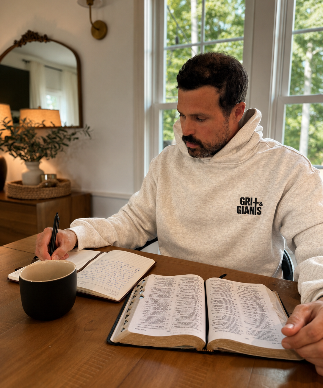Man wearing a white heather Grit & Giants Victory Hoodie while reading the Bible and writing at a table.