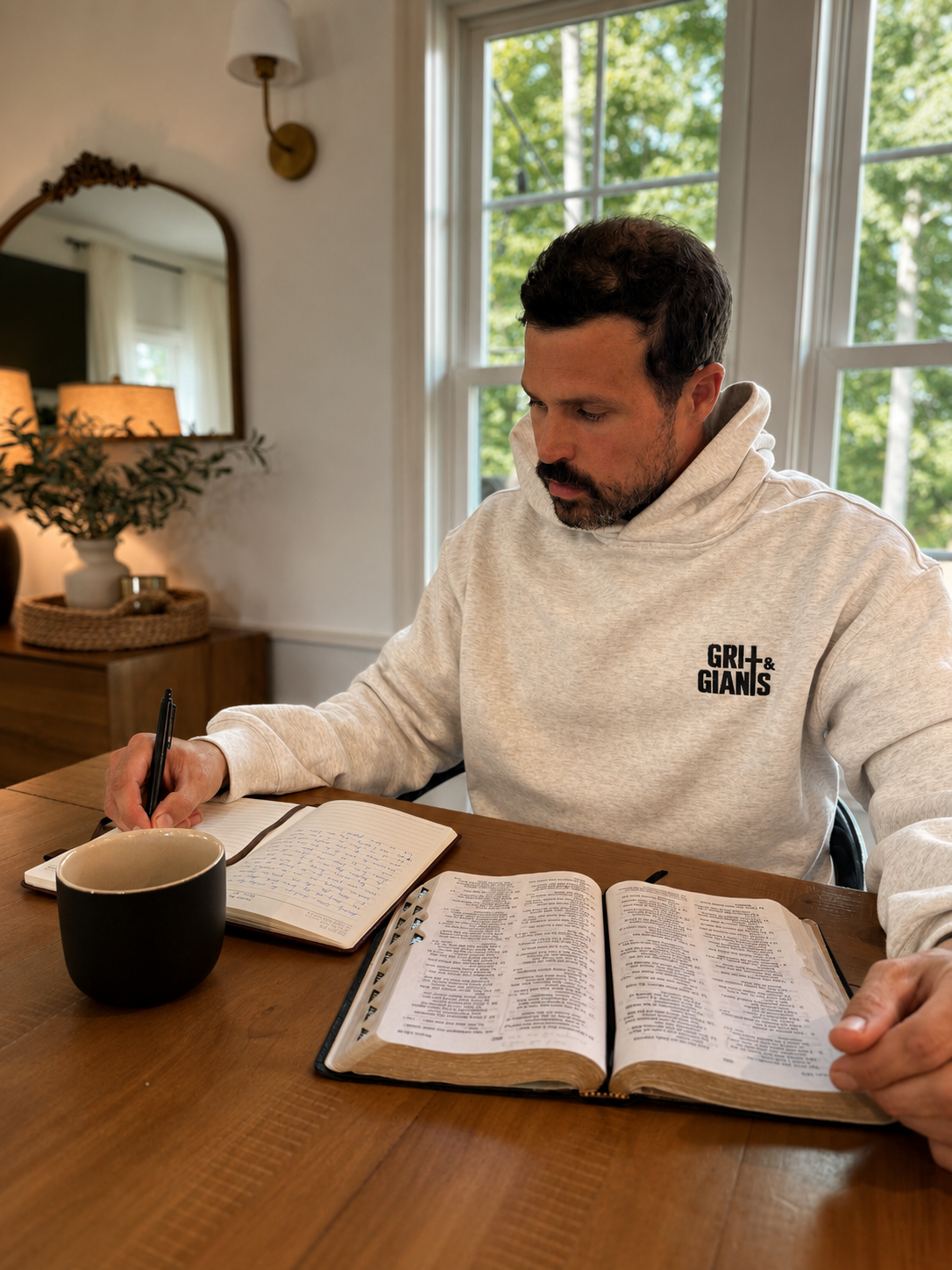 Man wearing a white heather Grit & Giants Victory Hoodie while reading the Bible and writing at a table.
