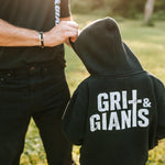 Boy wearing a black Grit & Giants youth hoodie outdoors with his father.