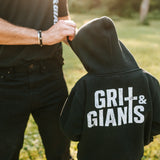 Boy wearing a black Grit & Giants youth hoodie outdoors with his father.