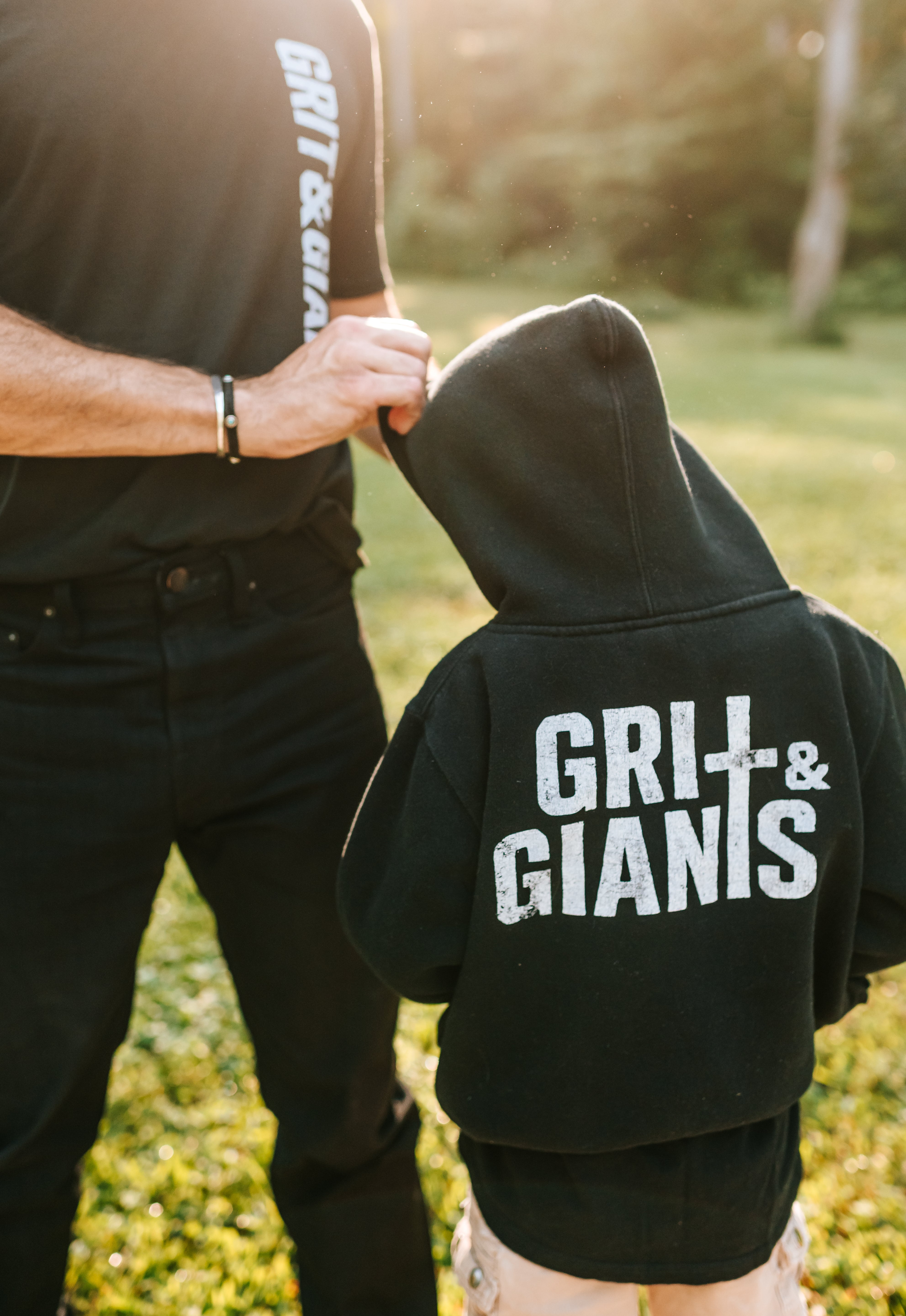 Boy wearing a black Grit & Giants youth hoodie outdoors with his father.