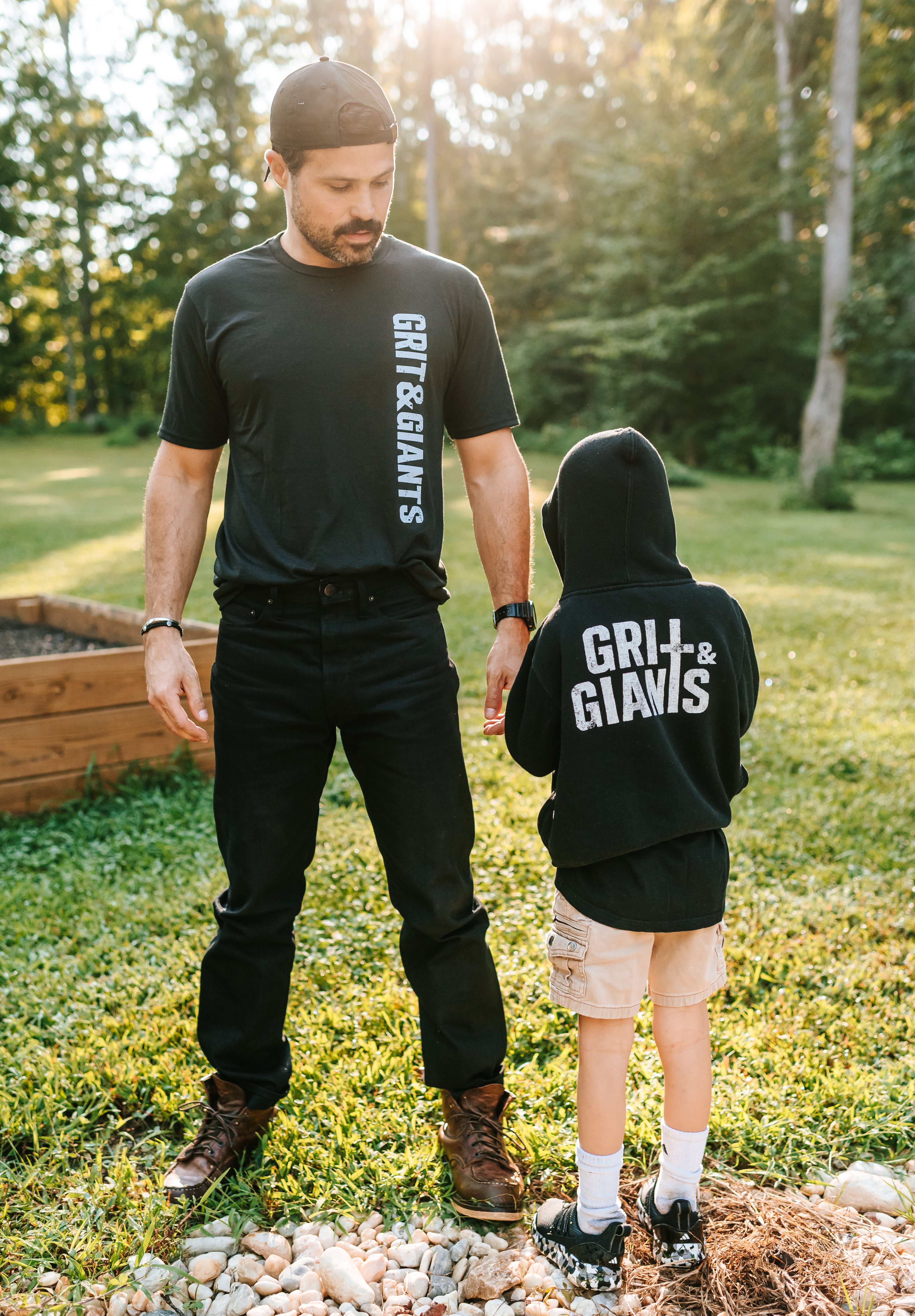 Father standing outdoors with his son wearing a black Grit & Giants youth hoodie.