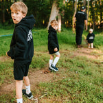 Boys wearing black Grit & Giants youth hoodies while walking outdoors with their father.