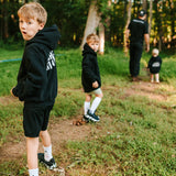 Boys wearing black Grit & Giants youth hoodies while walking outdoors with their father.