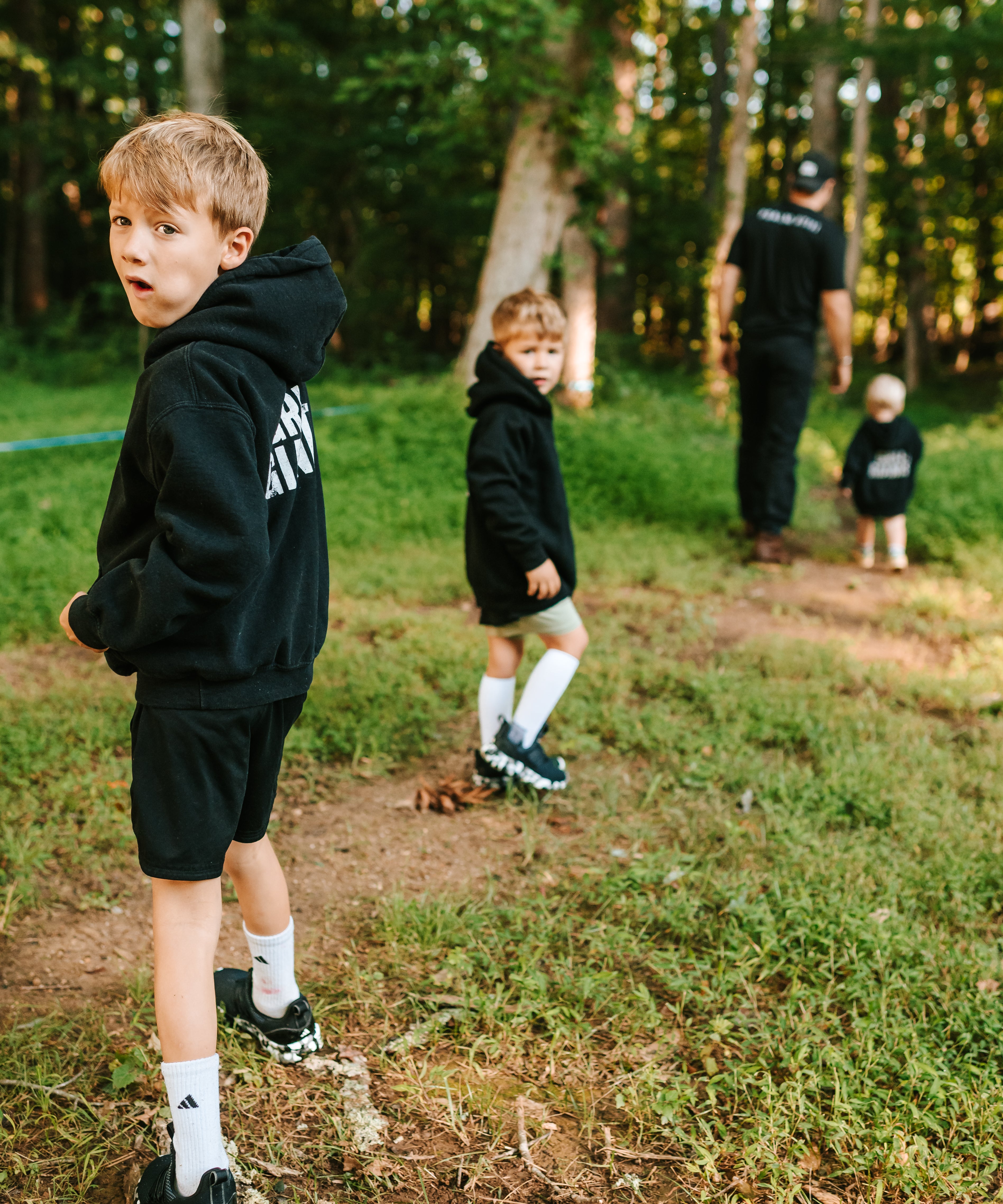 Boys wearing black Grit & Giants youth hoodies while walking outdoors with their father.