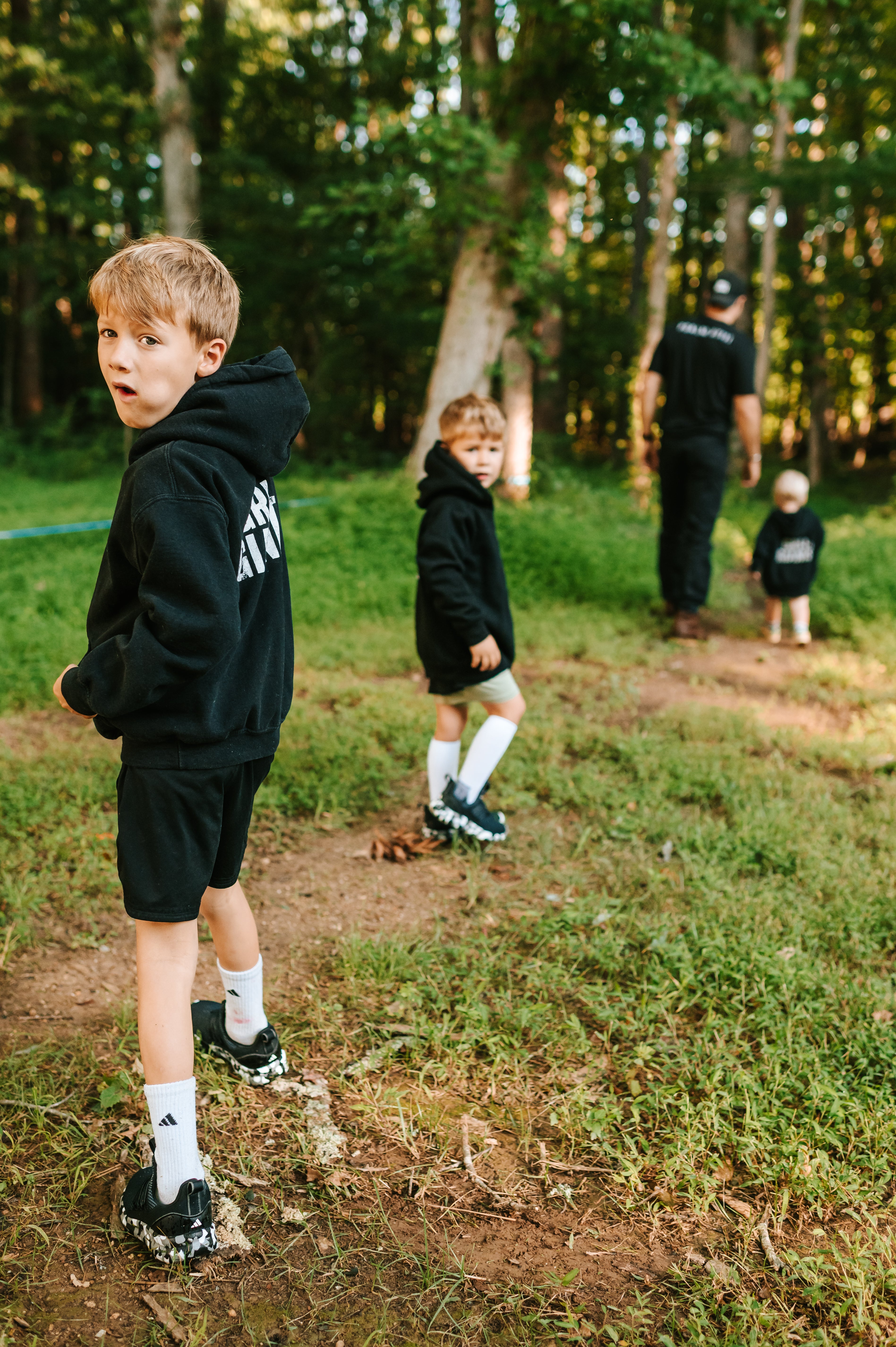 Boys wearing black Grit & Giants youth hoodies while walking outdoors with their father.