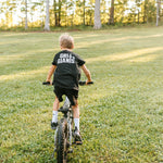 Boy riding a bike across the grass wearing a black Grit & Giants youth tee.