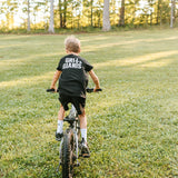 Boy riding a bike across the grass wearing a black Grit & Giants youth tee.