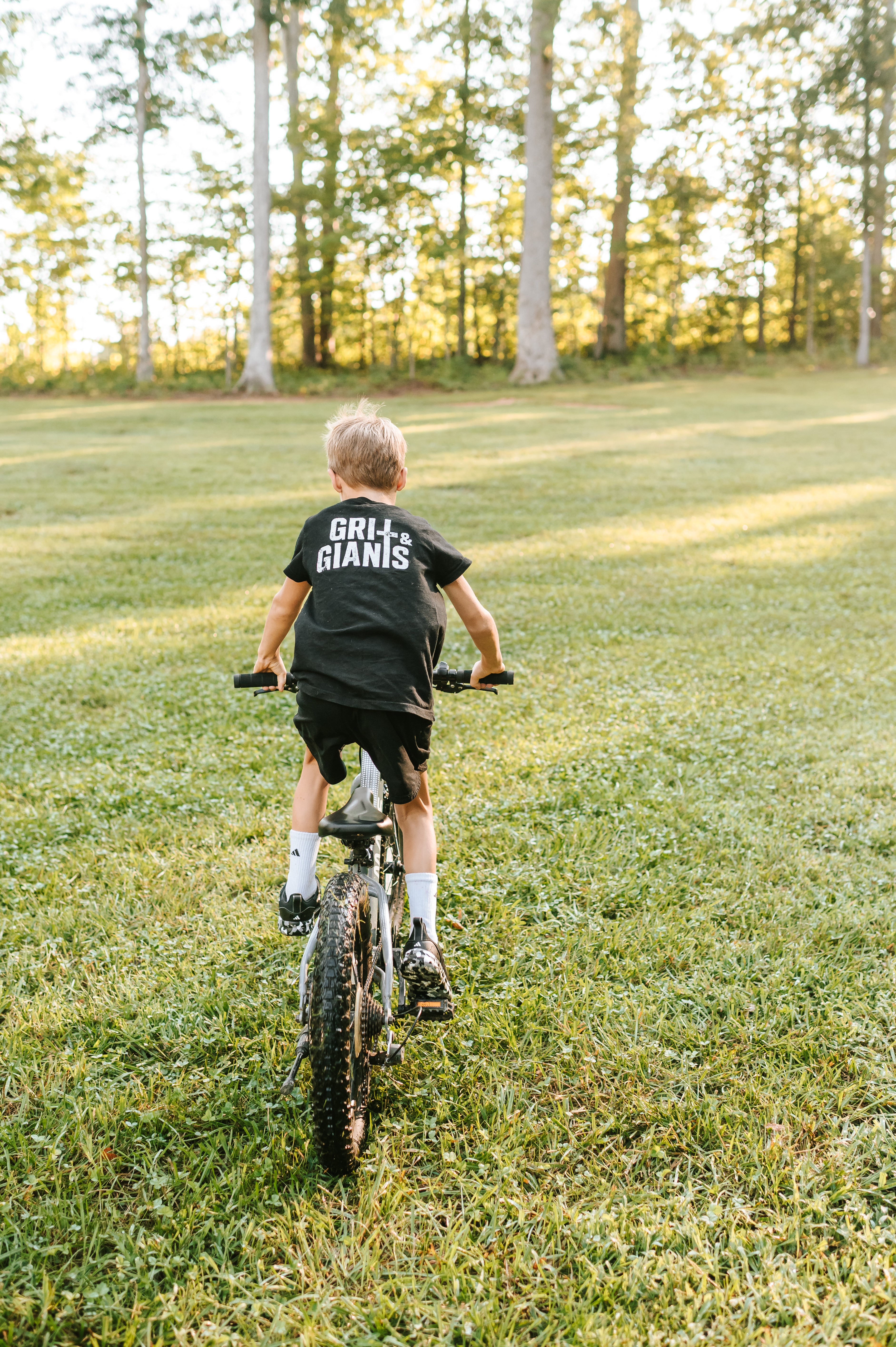 Boy riding a bike across the grass wearing a black Grit & Giants youth tee.
