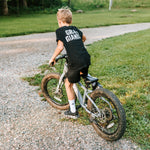 Boy wearing a black Grit & Giants youth tee while riding his bike outdoors.