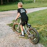 Boy wearing a black Grit & Giants youth tee while riding his bike outdoors.
