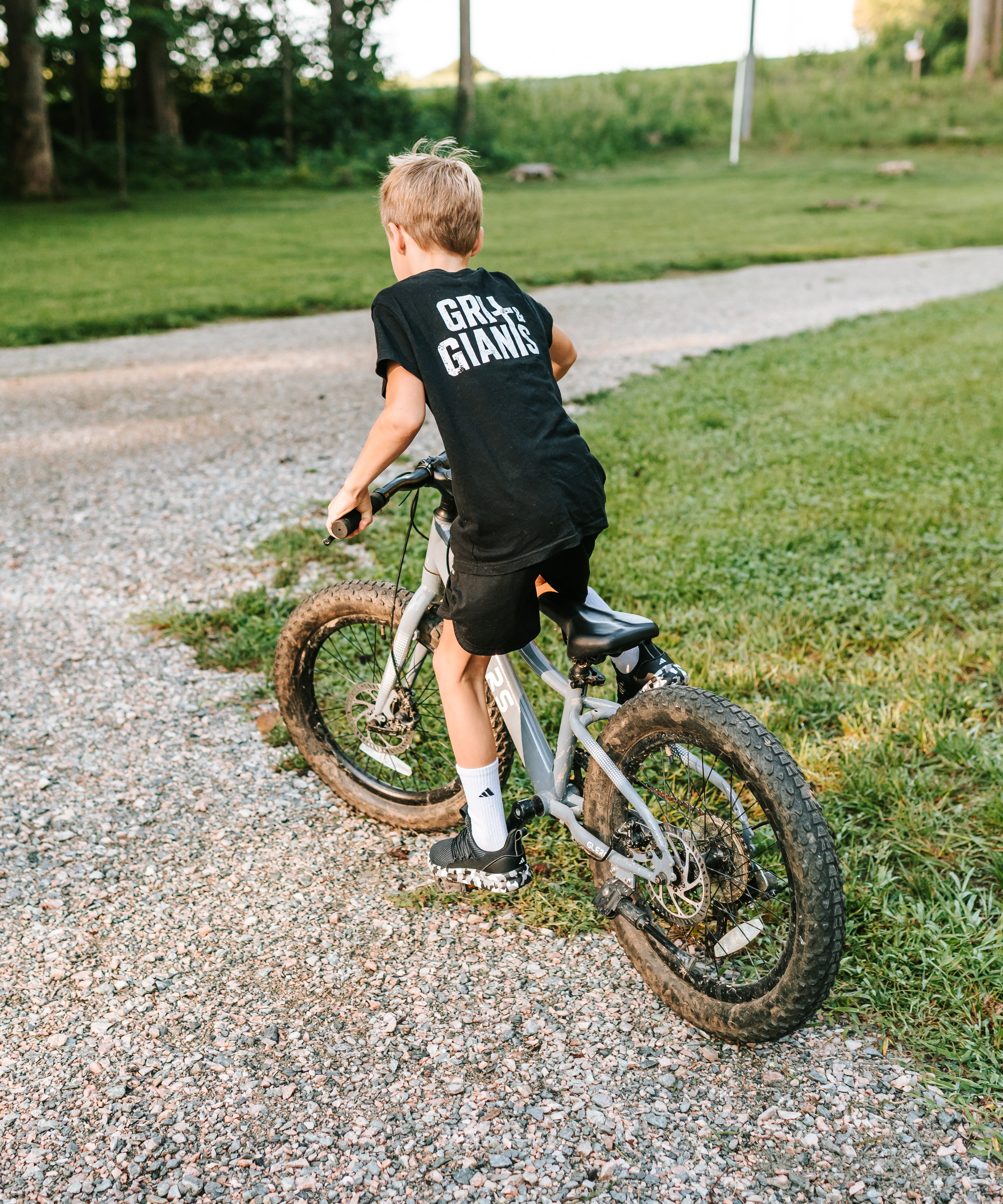 Boy wearing a black Grit & Giants youth tee while riding his bike outdoors.