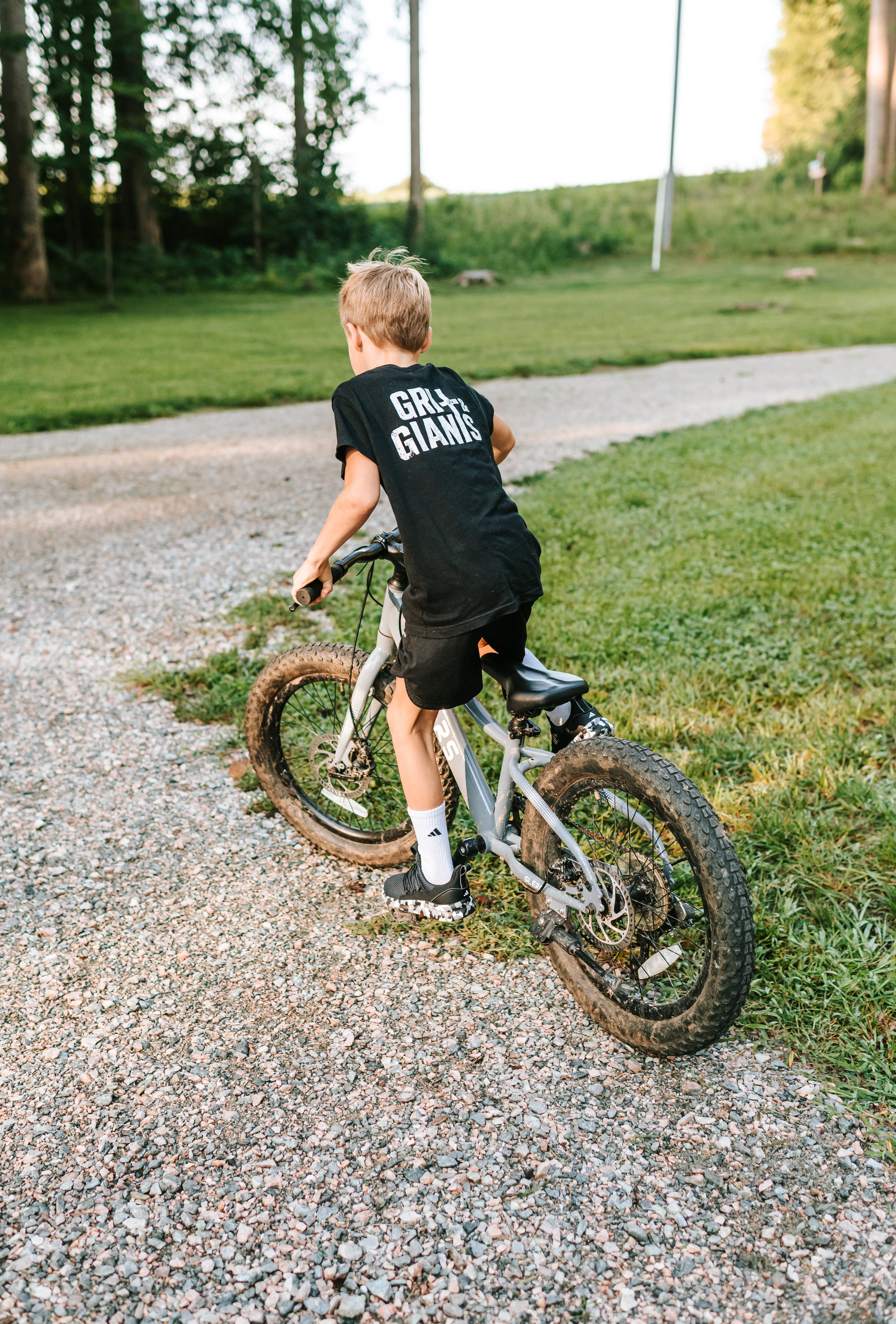 Boy wearing a black Grit & Giants youth tee while riding his bike outdoors.