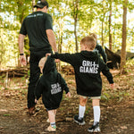 Two boys wearing black Grit & Giants youth and toddler hoodies while walking through the woods.