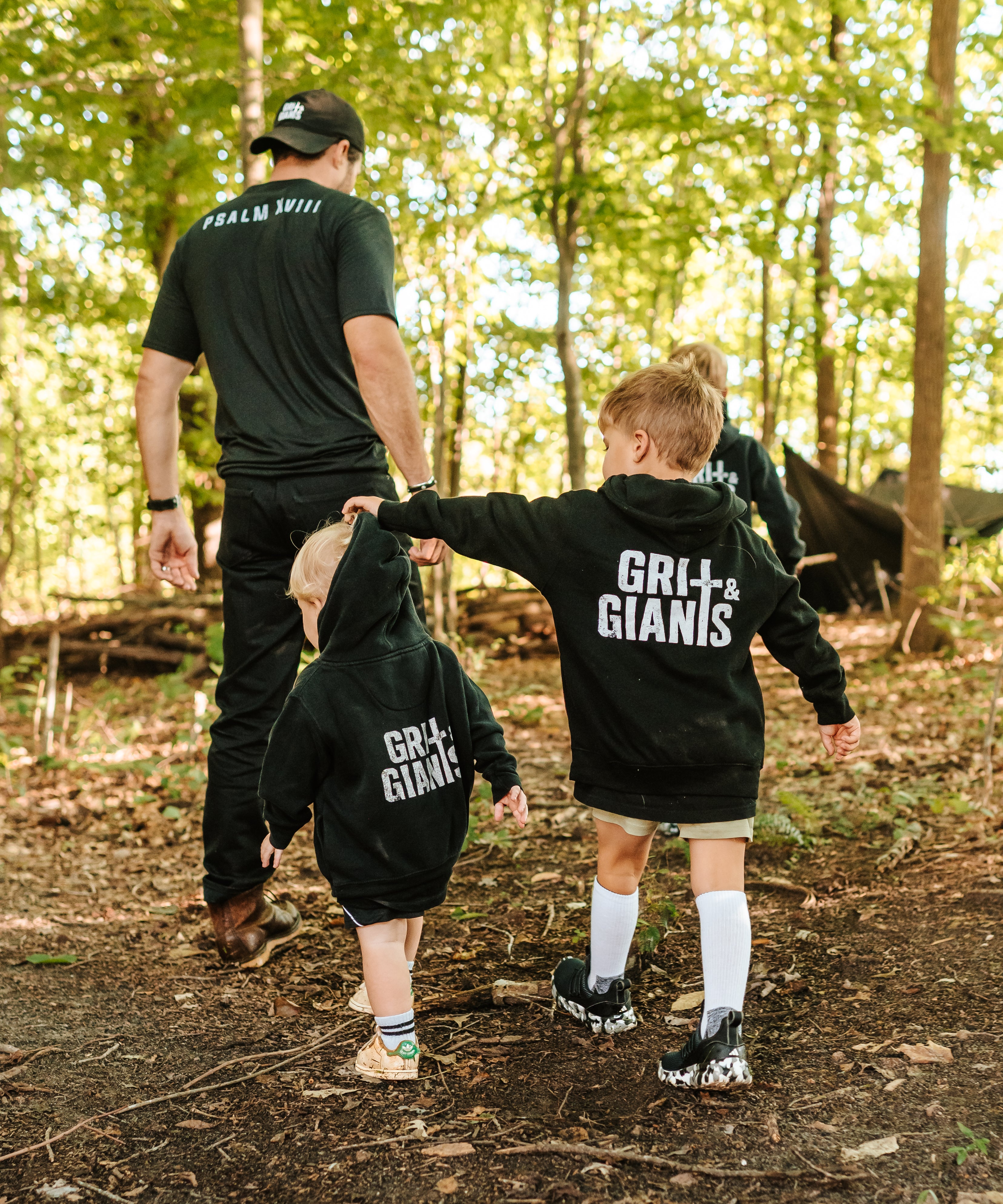 Two boys wearing black Grit & Giants youth and toddler hoodies while walking through the woods.