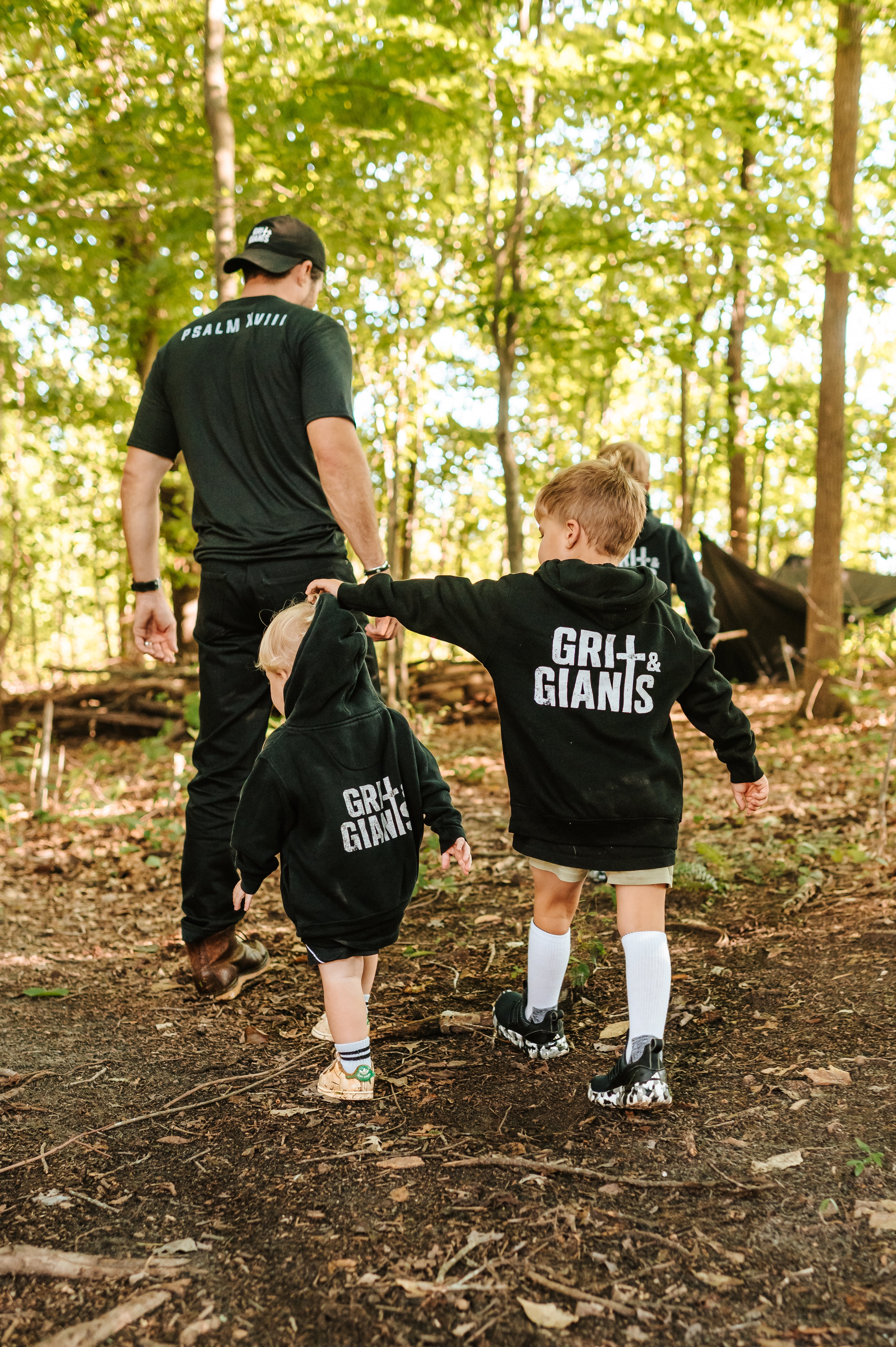 Two boys wearing black Grit & Giants youth and toddler hoodies while walking through the woods.